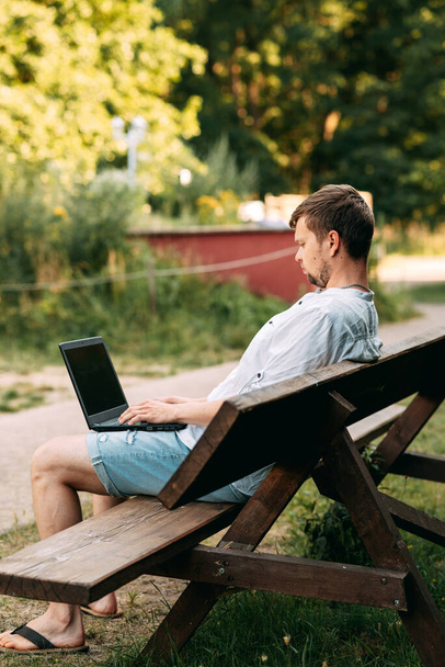 Portrait of a handsome man working with laptop sitting on a bench - Zdjęcie, obraz