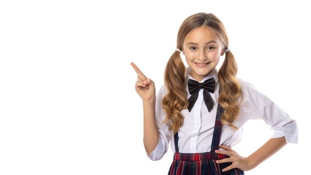 Portrait of positive school girl, pointing index finger copy space. Promoter isolated over white color background - Foto, imagen
