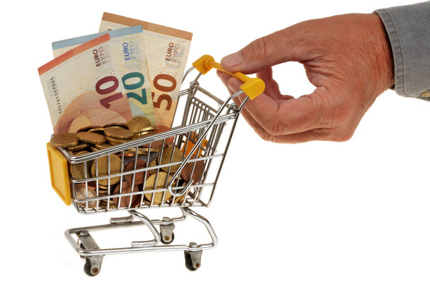 Ostovoimakonsepti, jossa supermarketin kärry on täynnä euroja ja jossa käsi työntää sen kiinni valkoisella pohjalla - Valokuva, kuva