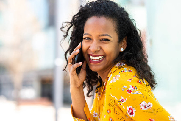 Закрыть портрет красивой молодой африканской женщины, разговаривающей по мобильному телефону и улыбающейся на улице - Фото, изображение