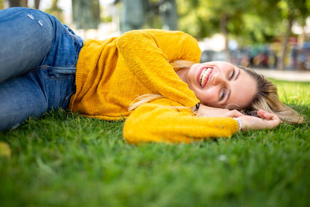 Portrait of a beautiful young woman lying on grass outside and smiling - Fotoğraf, Görsel