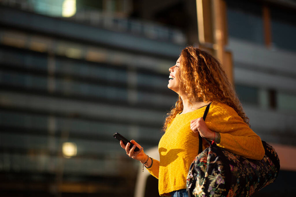 Side muotokuva hymyilevä nuori latino nainen kävely laukku ja matkapuhelin kaupungin ulkopuolella - Valokuva, kuva