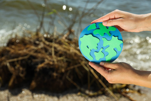 Planeta de papel Terra em mãos no fundo de uma praia poluída - Foto, Imagem