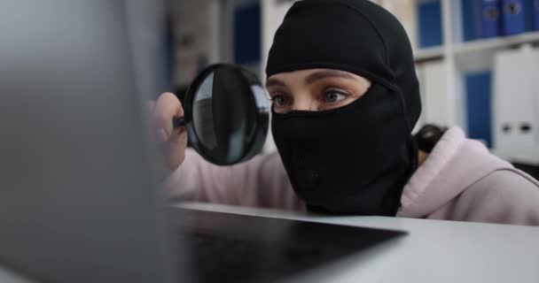 Woman hacker in balaclava near laptop, close-up, shallow focus. Internet fraud, theft of crypto assets - Imágenes, Vídeo
