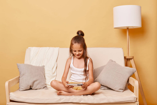 Cute brown haired little girl watching cartoons on her phone playing online video games wearing casual domestic clothing spending free time in internet. - Fotografie, Obrázek