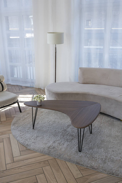 kreativní konferenční stolek a módní čalouněný nábytek v obývacím pokoji v prostorném open-plan apartmánu se stylovým moderním světlým designem za slunečného dne - Fotografie, Obrázek