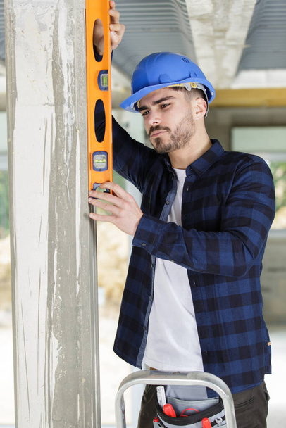 handsome builder posing with spirit level at construction site - Photo, Image