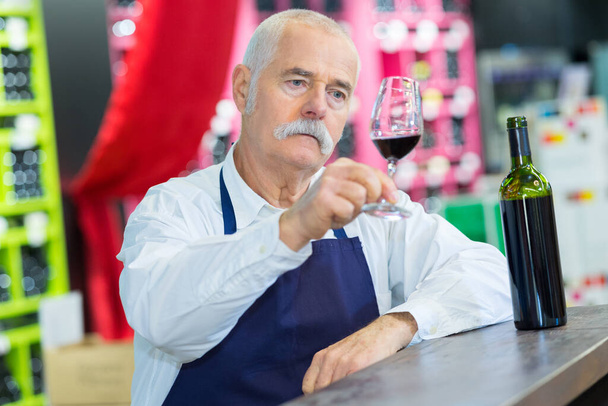 propietario de la tienda de vinos senior mirando el vino tinto - Foto, imagen