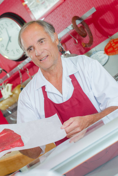 Old butcher serving a client - Foto, afbeelding