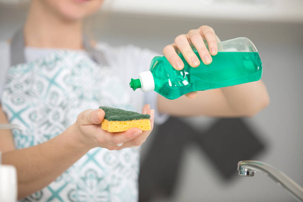 woman pouring washing up liquid on to a sponge - Foto, Imagen