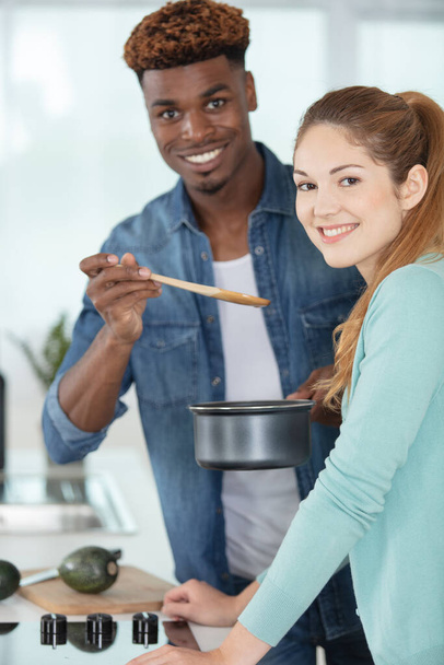 mixed-race couple tasting food on wooden spoon - Foto, afbeelding