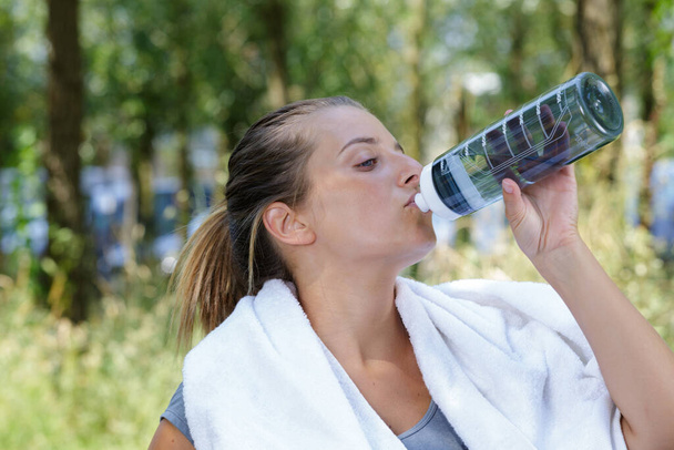 woman drinking water from bottle after exercising outdoors - 写真・画像