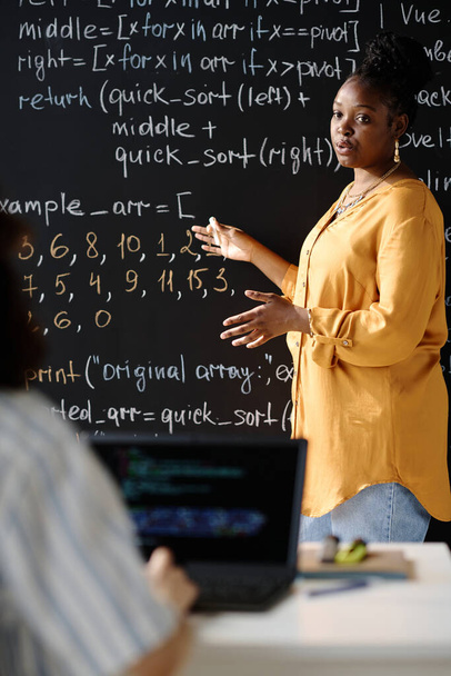 Vertical image of African American tutor pointing at blackboard and teaching IT to student at lesson - Φωτογραφία, εικόνα