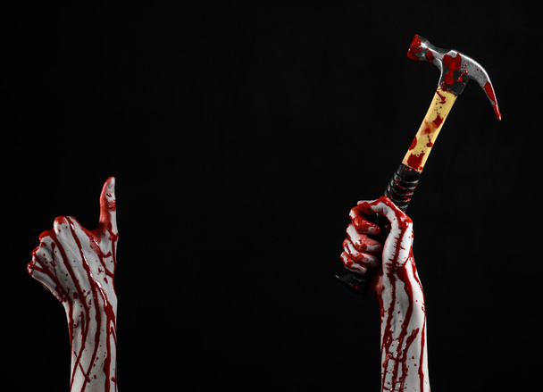 Bloody halloween theme: bloody hand holding a bloody hammer isolated on a black background - Foto, Bild