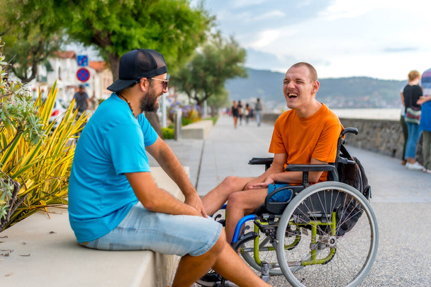Una persona disabile in sedia a rotelle con un amico in vacanza estiva si diverte a ridere molto - Foto, immagini
