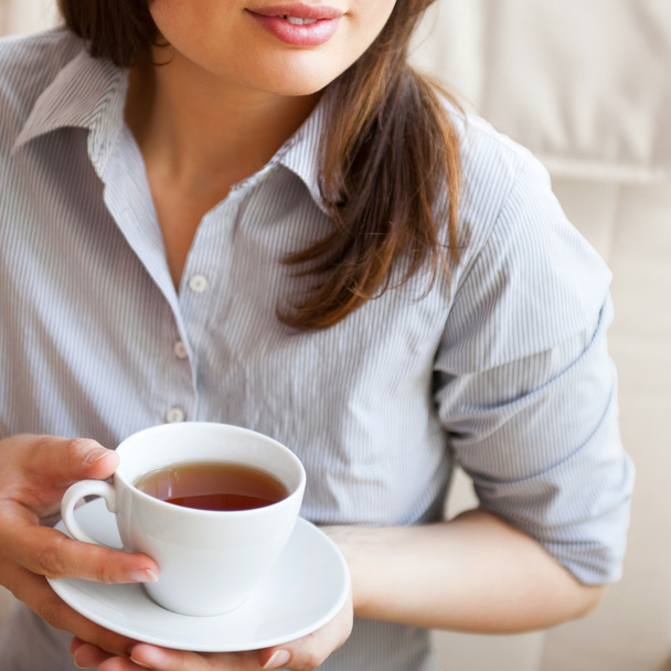 Egy fiatal nő otthon teát kortyolgat egy csészéből. - Fotó, kép