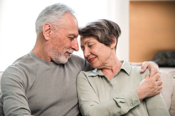 Portrait of mature couple hugging, spending free time at home. Smiling aged wife and husband, enjoying tender moment together. Eternal love and support in relationship. - Photo, Image