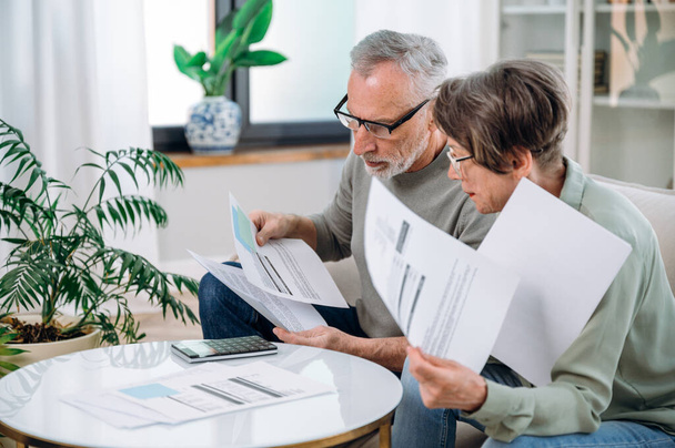 Elderly couple checking documents with tax and internal bills, making payments and discussing budget. Family calculating funds for purchase new home or car. - Photo, Image