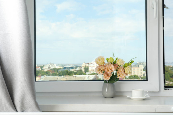 A pot of coffee and a vase of flowers on the windowsill with a view of the city - 写真・画像
