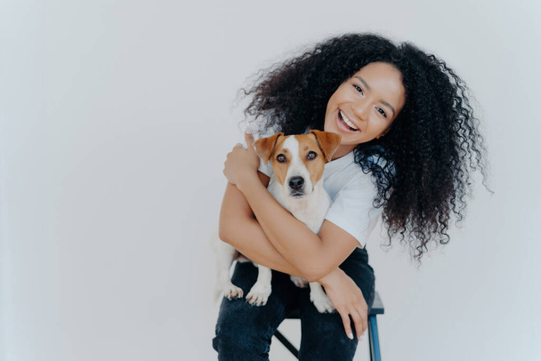 Curly girl smiles, embraces beloved dog, enjoys good time together, showcasing their close relationship. - Photo, Image