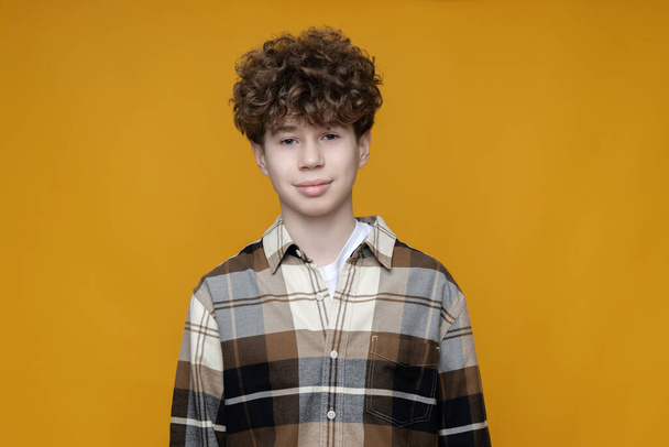 Curly teenager in a shirt on a yellow background - Фото, зображення