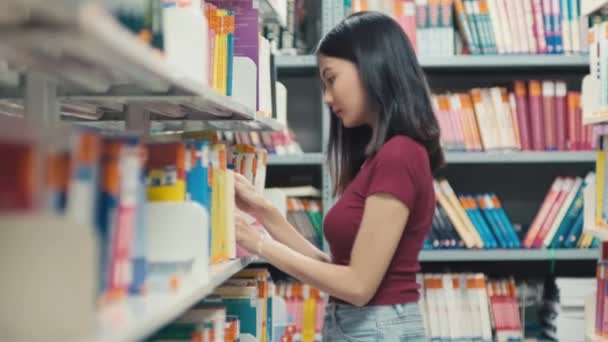 Střední záběr ženského prváka hledajícího knihu v knihovně - Záběry, video