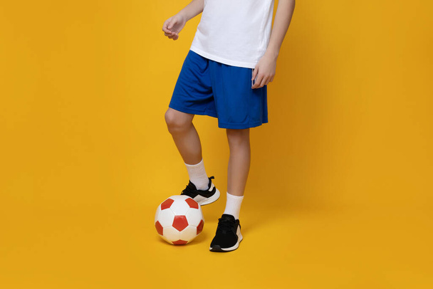 Legs of a teenager with a ball on a yellow background - Foto, Imagen