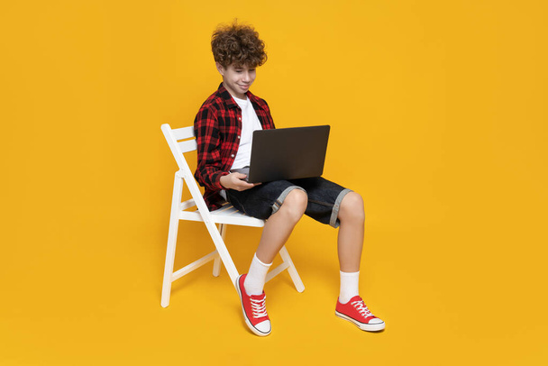 Attractive boy, teenager in stylish sitting on chair with laptop - Photo, Image