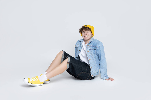 Attractive boy, teenager in stylish sitting on gray background - Foto, Imagen