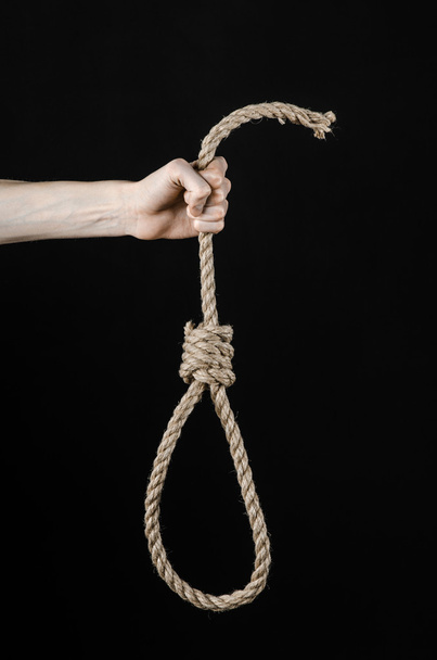 Lynching and suicide theme: man's hand holding a loop of rope for hanging on black isolated background - Foto, afbeelding