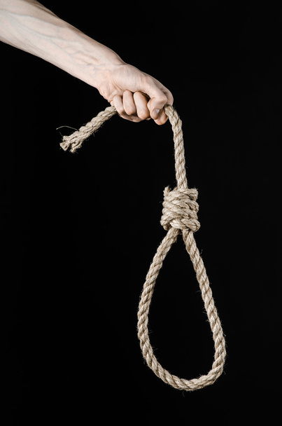 Lynching and suicide theme: man's hand holding a loop of rope for hanging on black isolated background - Фото, изображение