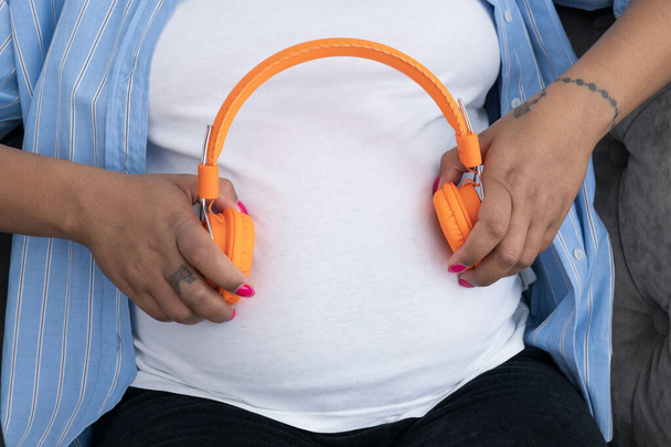 A pregnant woman puts headphones to her stomach - Zdjęcie, obraz
