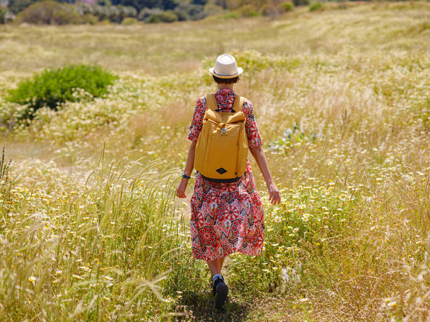 ギリシャのロードス島への夏の旅行。民族衣装や黄色のバックパックを着た若いアジアの女性がロードスの街を見渡すために歩く。観光、休暇、ソロ旅行と発見の概念 - 写真・画像