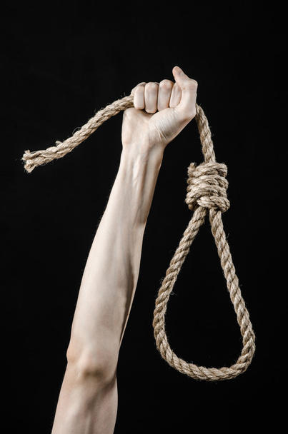 Lynching and suicide theme: man's hand holding a loop of rope for hanging on black isolated background - Fotoğraf, Görsel