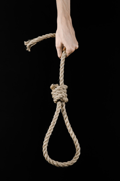 Lynching and suicide theme: man's hand holding a loop of rope for hanging on black isolated background - 写真・画像