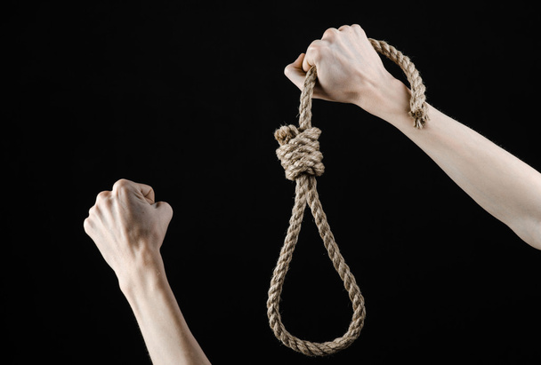 Lynching and suicide theme: man's hand holding a loop of rope for hanging on black isolated background - Foto, afbeelding