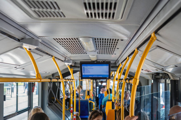 A dynamic urban scene of a group of people in motion on a city bus. The monitor screen and the lamp on the ceiling create a contrast with the sunny street outside, windows reflect. Trendy urban scene - Photo, Image