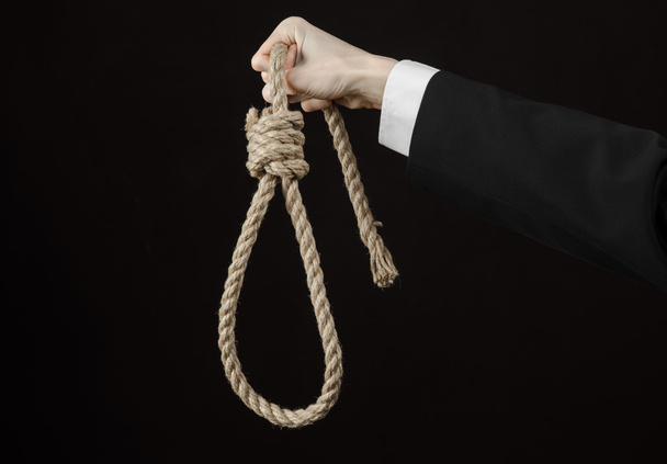 Suicide and business topic: Hand of a businessman in a black jacket holding a loop of rope for hanging on black isolated background - Fotografie, Obrázek