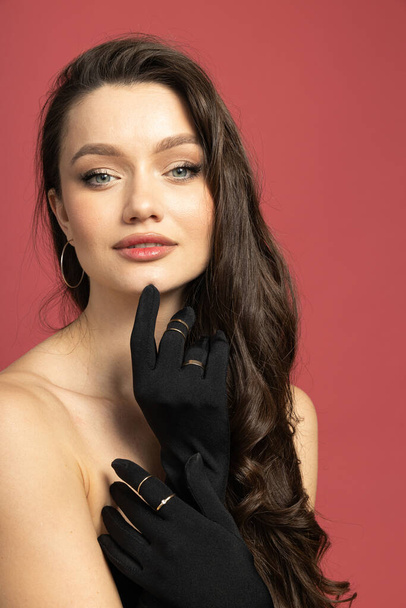 Portrait of a brunette in mittens with jewelry, on a pink background - Fotografie, Obrázek