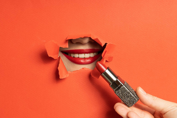 Close-up van vrouwelijke lippen in gescheurd papiergat met lippenstift - Foto, afbeelding