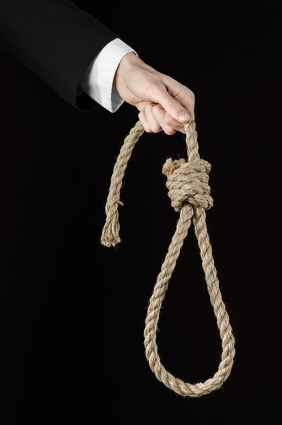 Suicide and business topic: Hand of a businessman in a black jacket holding a loop of rope for hanging on black isolated background - Foto, afbeelding