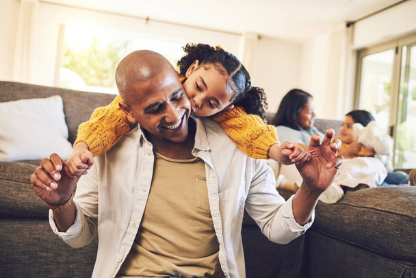 Happy, playing and a child with a kiss for a father, love and bonding together in a house. Smile, family and a girl and a young dad holding hands with a piggyback in the living room for a hug. - Photo, Image