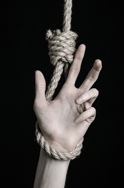 Suicide and depression topic: human hand hanging on rope loop on a black background - Foto, afbeelding