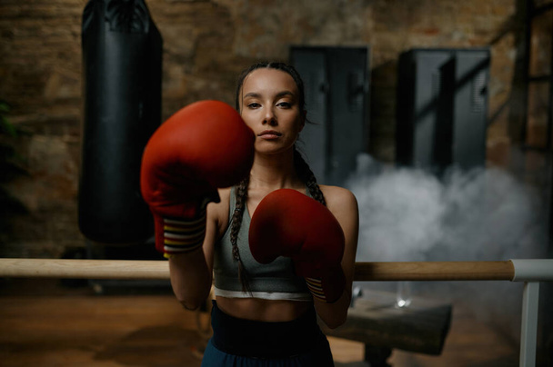 Mujer boxeadora bastante deportiva golpeando con guantes de boxeo durante el entrenamiento retrato de tiro en la cabeza. Preparación de la competición deportiva, afición y concepto de éxito - Foto, imagen