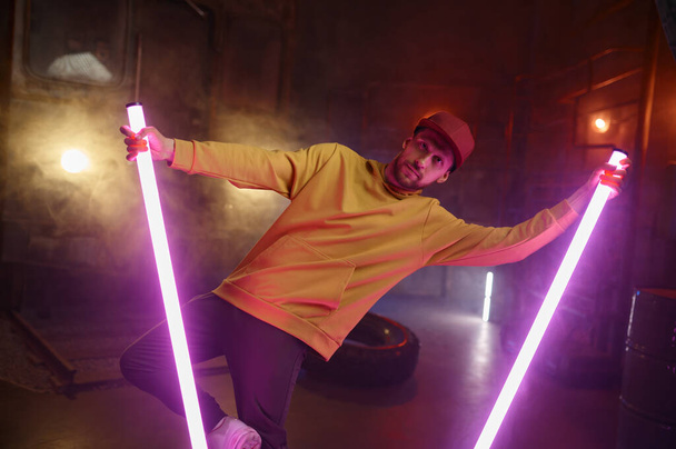 Творческий хипстер-брейкдансер позирует танцуя со светящимися светодиодными лампами на чердаке подпольной студии - Фото, изображение