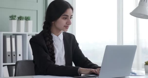Femme d'affaires indienne élégante, travaille avec diligence sur son ordinateur portable, en tapant sur le clavier avec concentration et précision. Positivité rayonnante, elle se tourne vers la caméra, son visage orné d'un large sourire. - Séquence, vidéo