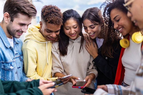 Jugendliche, die gemeinsam im Freien mit dem Handy telefonieren. Junge Gruppe von Gen-Tech-Studentenkollegen, die Spaß daran haben, Social-Media-Inhalte auf Smartphone-Applikationen anzusehen. Süchtige Teenager telefonieren miteinander. - Foto, Bild