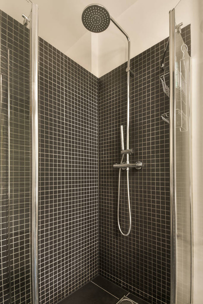 une salle de bain carrelée noire et blanche avec une pomme de douche sur le côté gauche, WC au milieu à droite - Photo, image