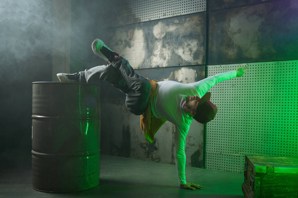 Mężczyzna break tancerz występujący na scenie strychu w zielonym świetle neonu. Profesjonalny stylowy facet breakdancer akrobata robi sztuczki w ekspresyjnym tańcu. Kultura młodzieżowa i koncepcja freestyle - Zdjęcie, obraz