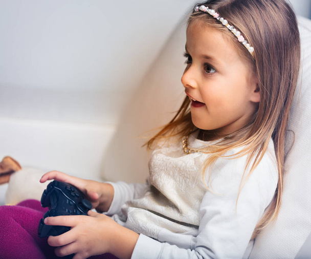 Ein kleines Mädchen erlebt spannende Herausforderungen beim Spielen von Videospielen zu Hause, beaufsichtigt von ihren Eltern - Foto, Bild